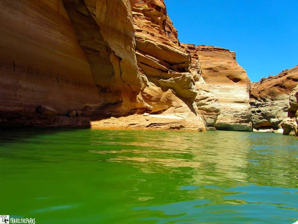View of Lake Powell with blue sky and rocky canyon walls reflected in greenish water.