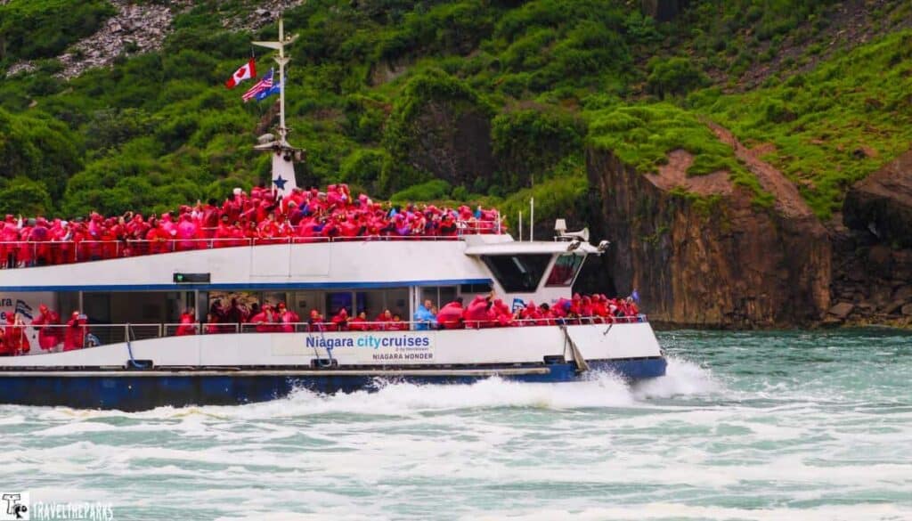 Niagara City Cruises boat filled with people in red ponchos near a green cliff at Niagara Falls.