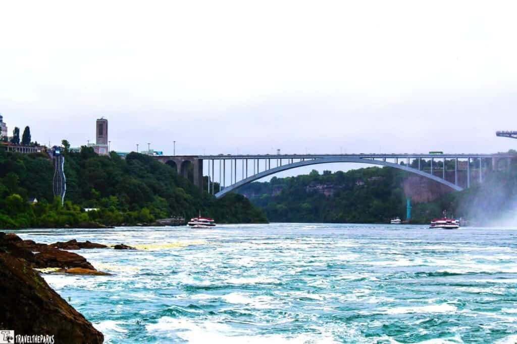 View of the Rainbow Bridge over the Niagara River with boats and mist in the background.