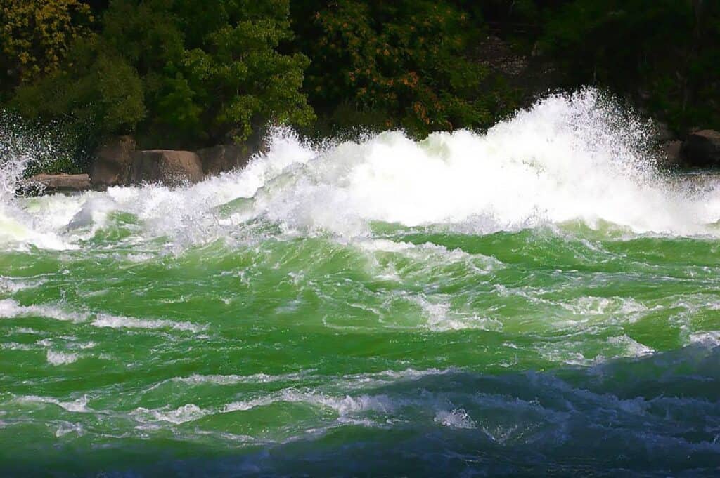Swirling blue-green waters of the Niagara River with rocky banks and a clear blue sky.