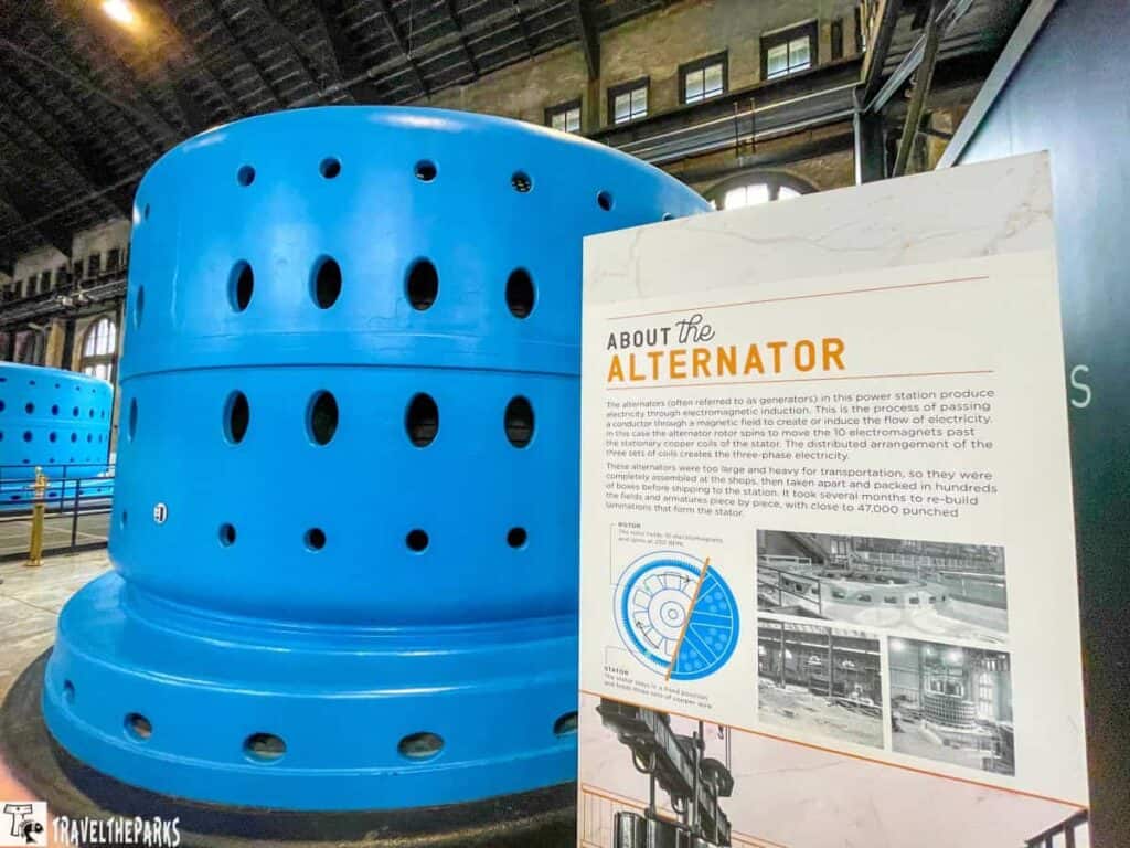Large blue cylindrical machine with an informational sign about the alternator inside a power station.