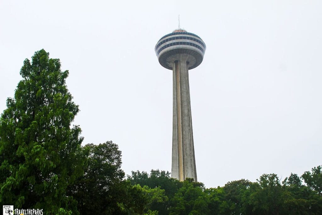 Skylon Tower in Niagara Falls against a gray sky, surrounded by green trees.