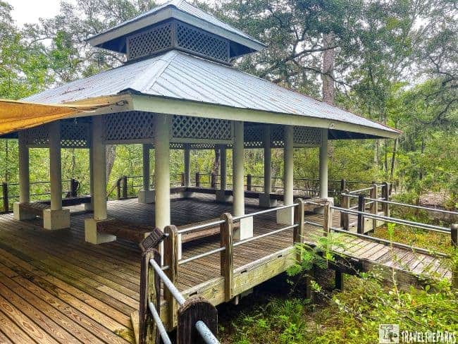 Wooden gazebo at Stephen Foster Folk Culture Center with a blue, multi-tiered roof and latticework, surrounded by trees.