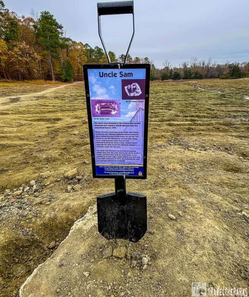 Sign about the Uncle Sam diamond on a shovel handle in a rocky field with autumn trees in the background.