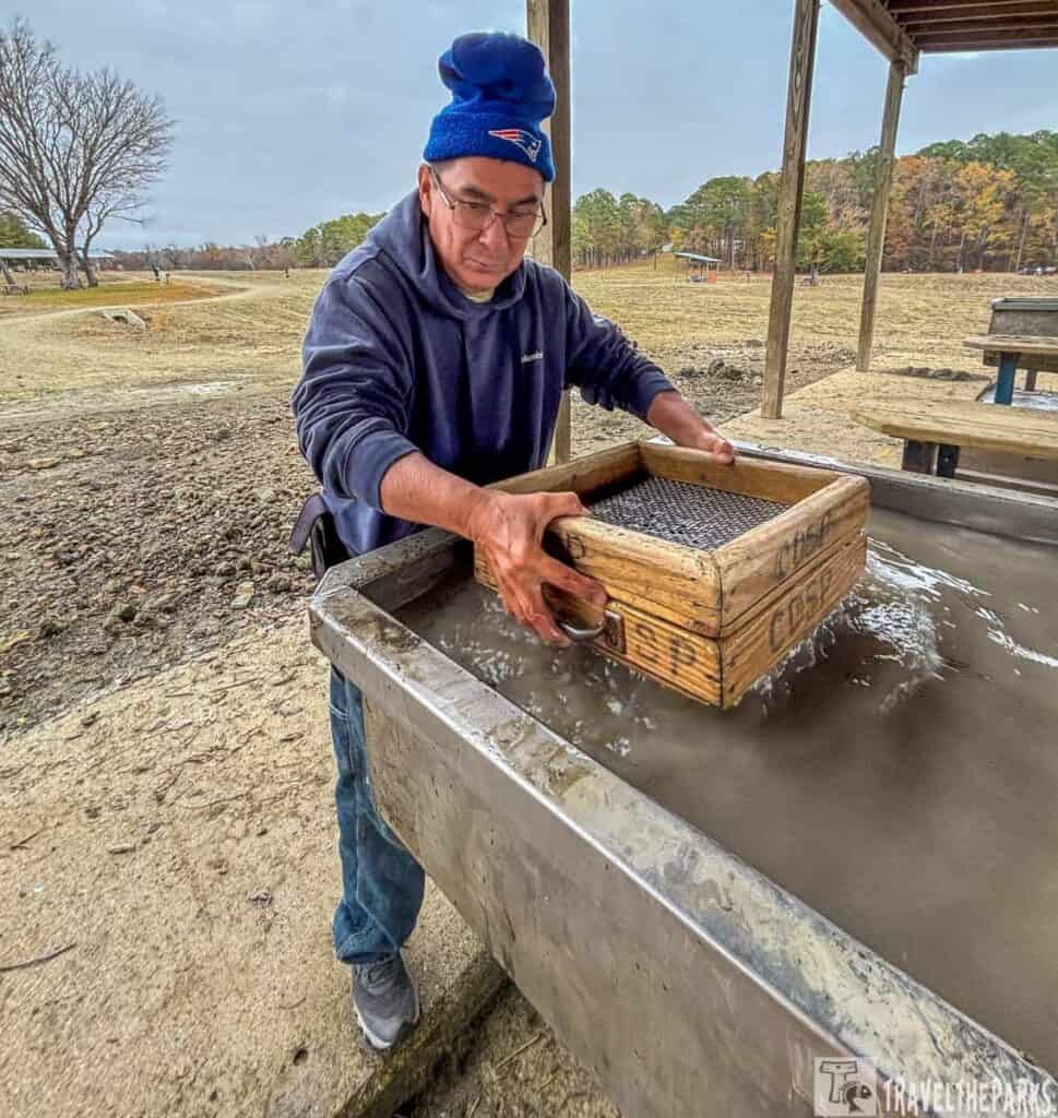 Person using a wooden sifting box at a water trough outdoors.