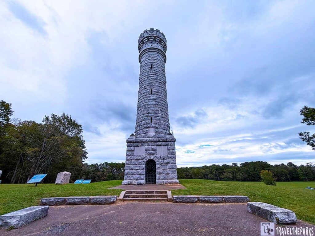 Wilder Brigade Tower: A tall cylindrical stone monument with a crenelated top in a grassy field, surrounded by trees.

