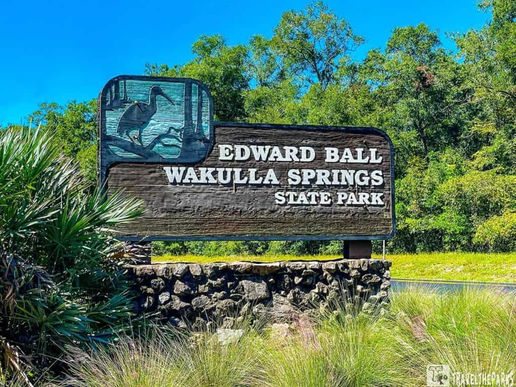 "Edward Ball Wakulla Springs State Park sign with bird relief, surrounded by trees and sky."