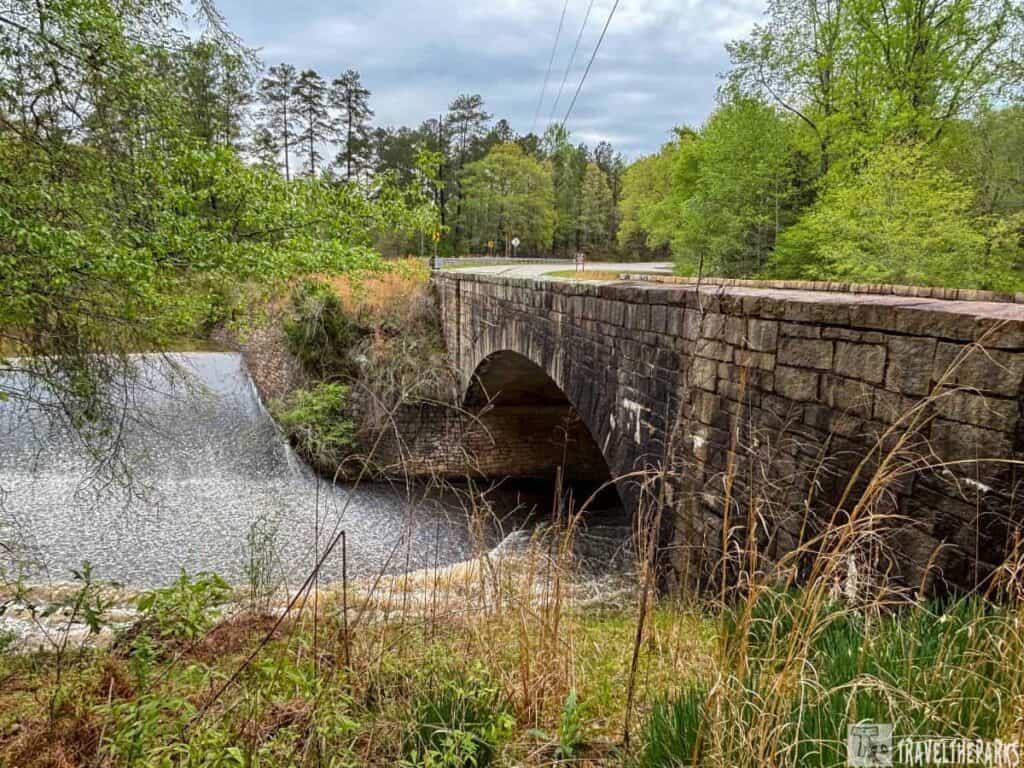 Stone bridge over a dam with greenery and trees.
