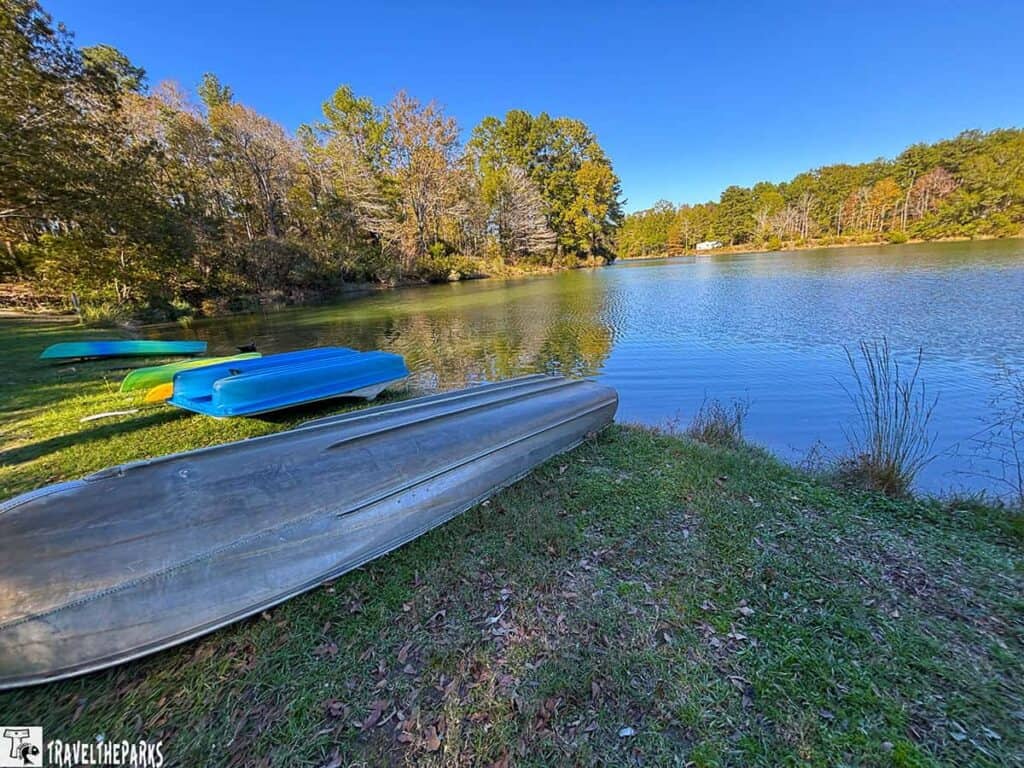 Overturned boats on a grassy bank by a calm lake under a clear blue sky.