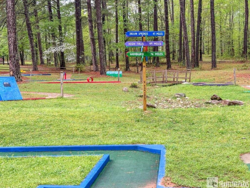 Mini-golf course with directional signs and tall pine trees.