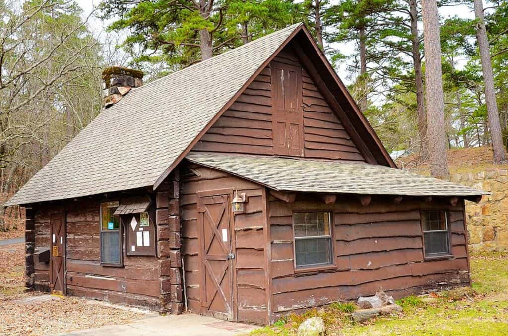 A rustic brown wooden cabin with a steep roof, surrounded by trees.