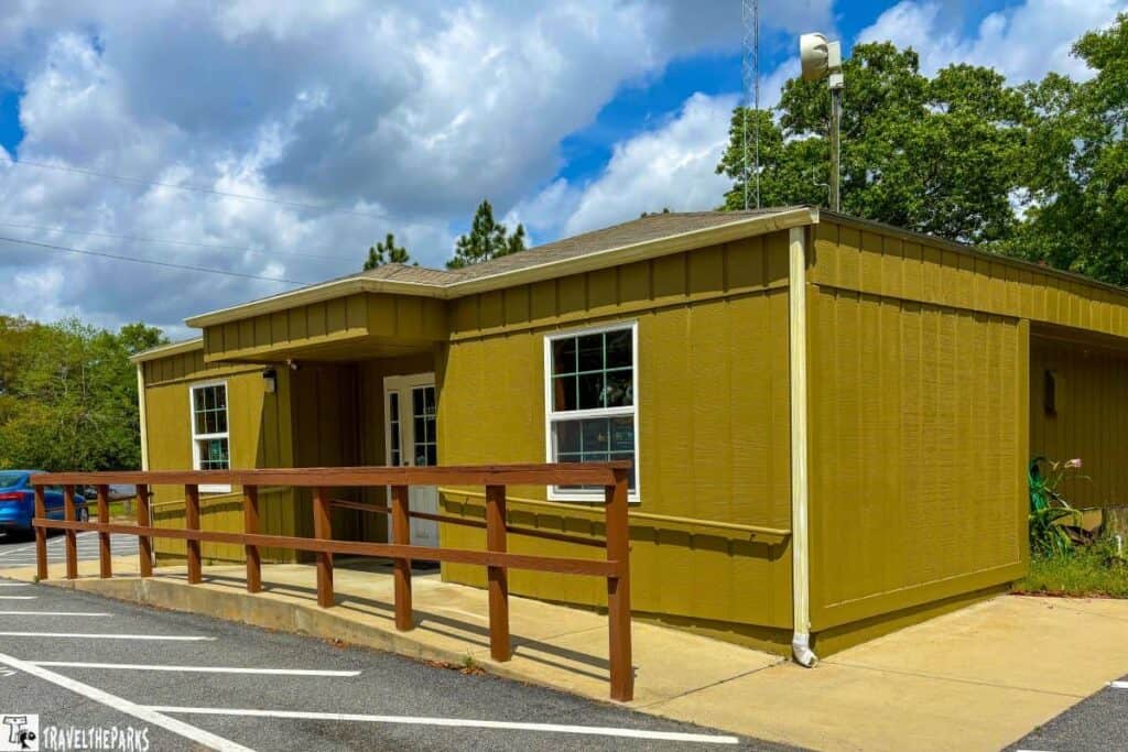 A small olive green building with a white trim, wooden ramp, and white doors.