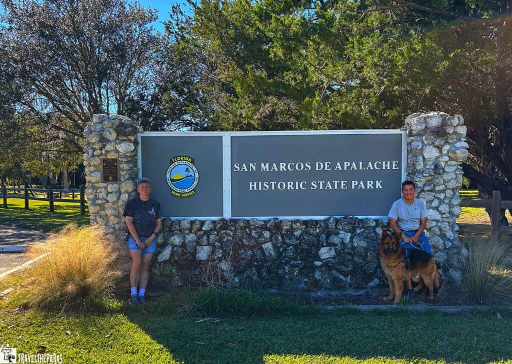 Stone monument sign for San Marcos de Apalache Historic State Park, with two people and a dog.