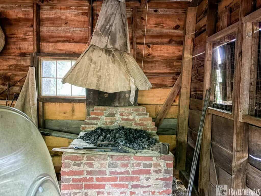Interior of a rustic workshop with a brick forge and wooden walls.