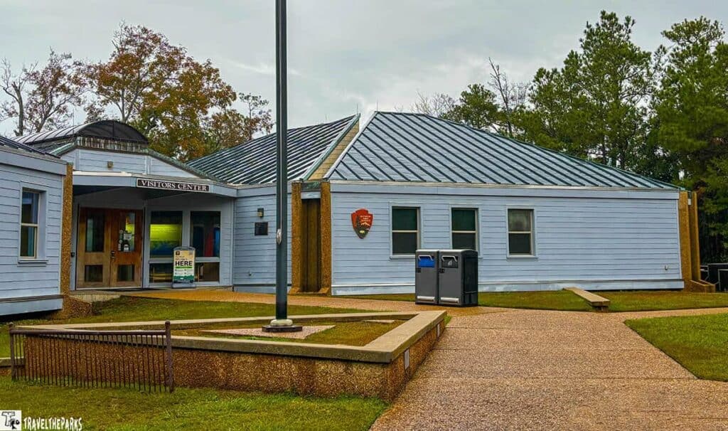 William M. Colmer Visitor's center with light blue siding, a sloped roof, and a double wooden door entrance labeled "VISITORS CENTER" in Davis Bayou.