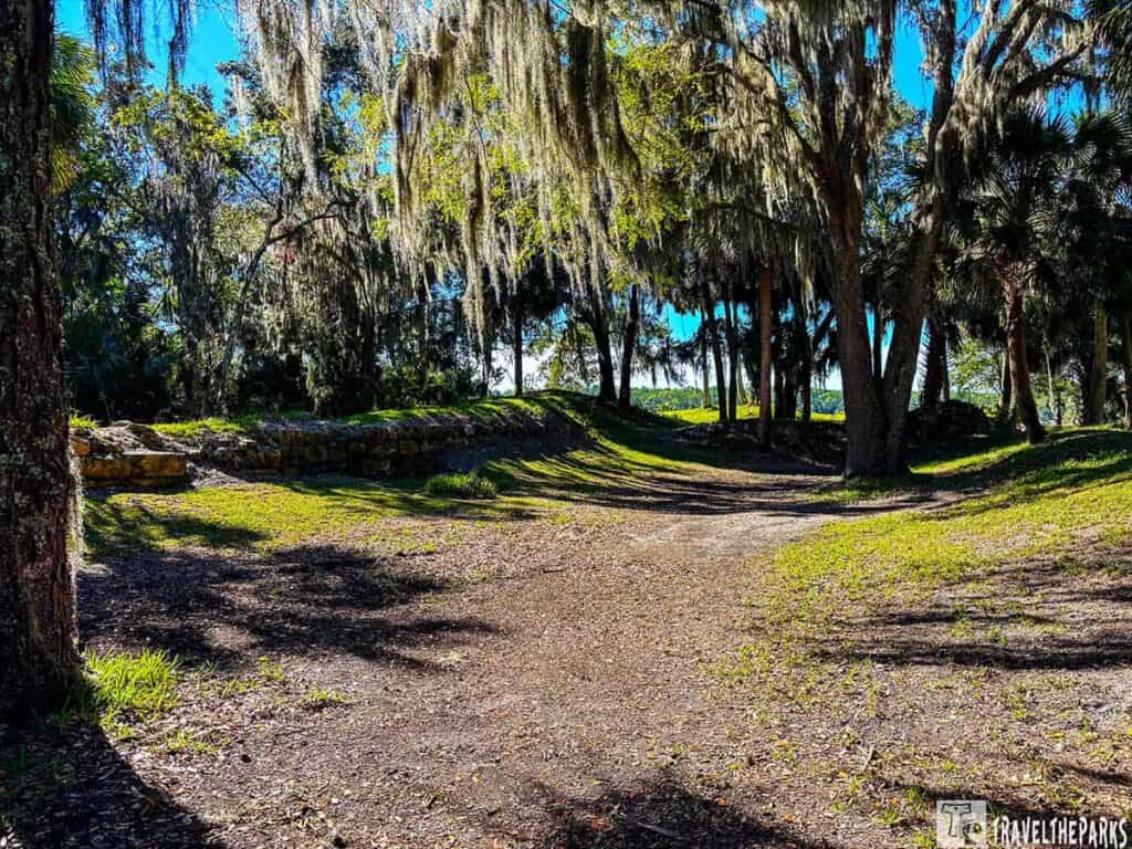 Dirt pathway leading to Confederate earthworks surrounded by trees with Spanish moss.