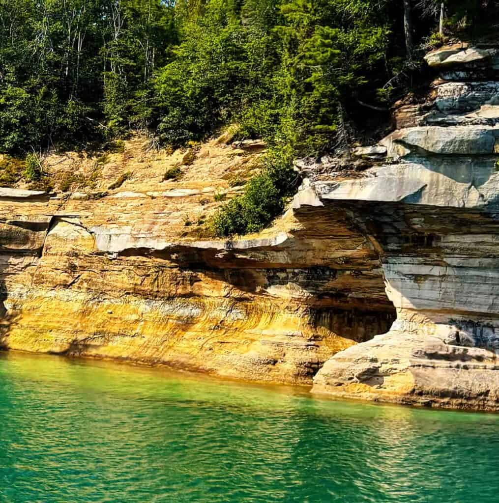 Cliffs and turquoise water at Pictured Rocks National Lakeshore with trees at the top.