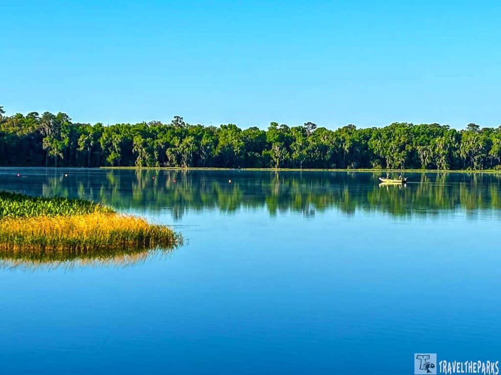 A tranquil lake scene with a boat, reflecting water, and green trees.