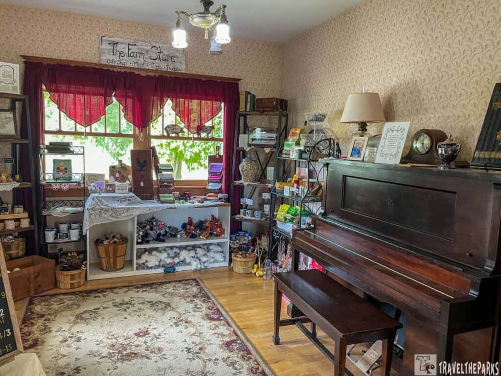 Interior of a cozy farm store with shelves of goods, a window with red curtains, a wooden piano, and vintage decor.