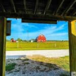 View of a farm with a red barn and windmill at Prophetstown State Park, framed by a wooden structure.