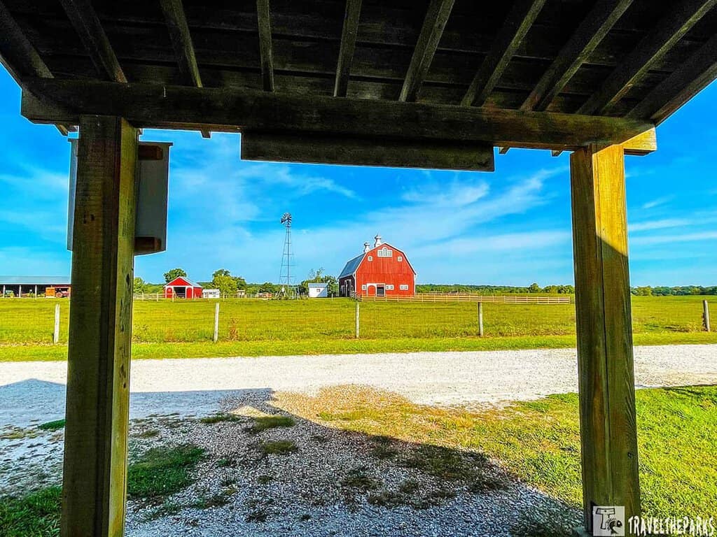 View of a farm with a red barn and windmill at Prophetstown State Park, framed by a wooden structure.