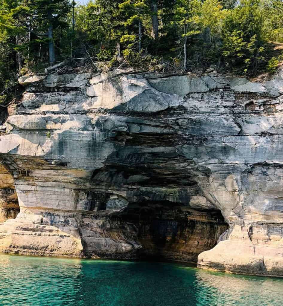 Rocky cliff with arch formation and turquoise water at Pictured Rocks National Shoreline.