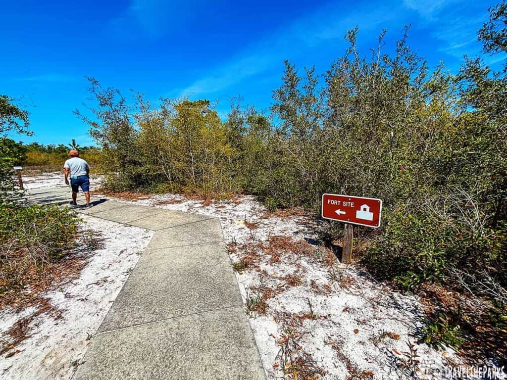 A person walking on a paved path towards a sign indicating "Fort Site" with an arrow.