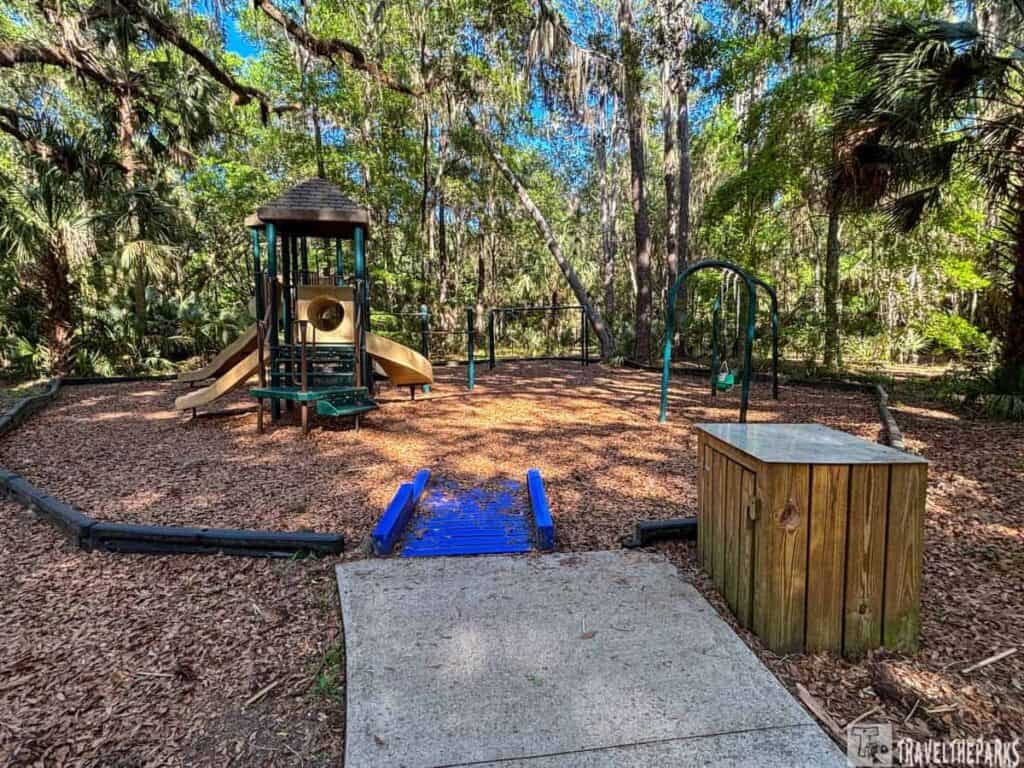 Playground with slides, swings, wood chip ground, and surrounding trees.