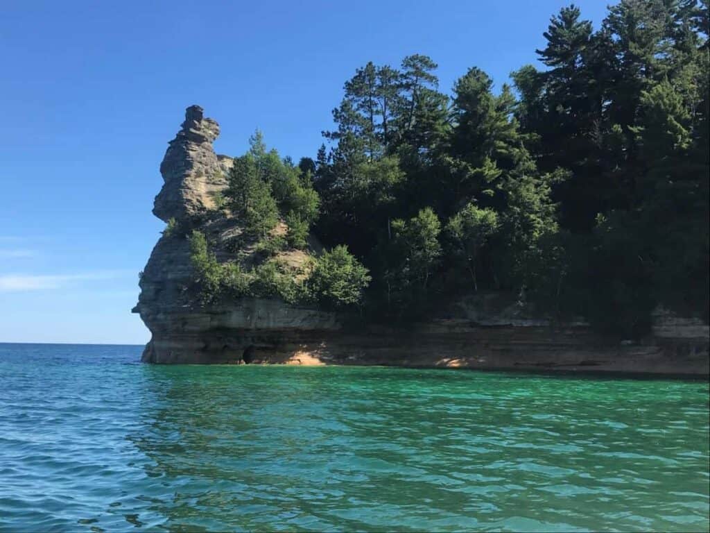Miners Castle rock formation at Pictured Rocks, with turquoise water and a backdrop of dense trees.
