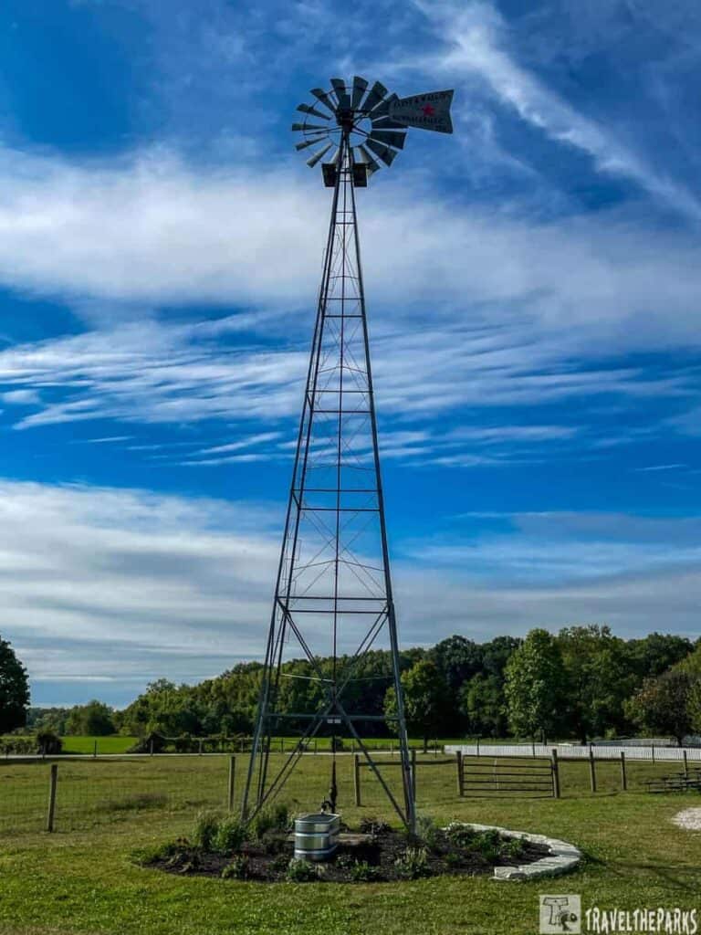 Tall windmill in a grassy field with blue sky and scattered clouds.