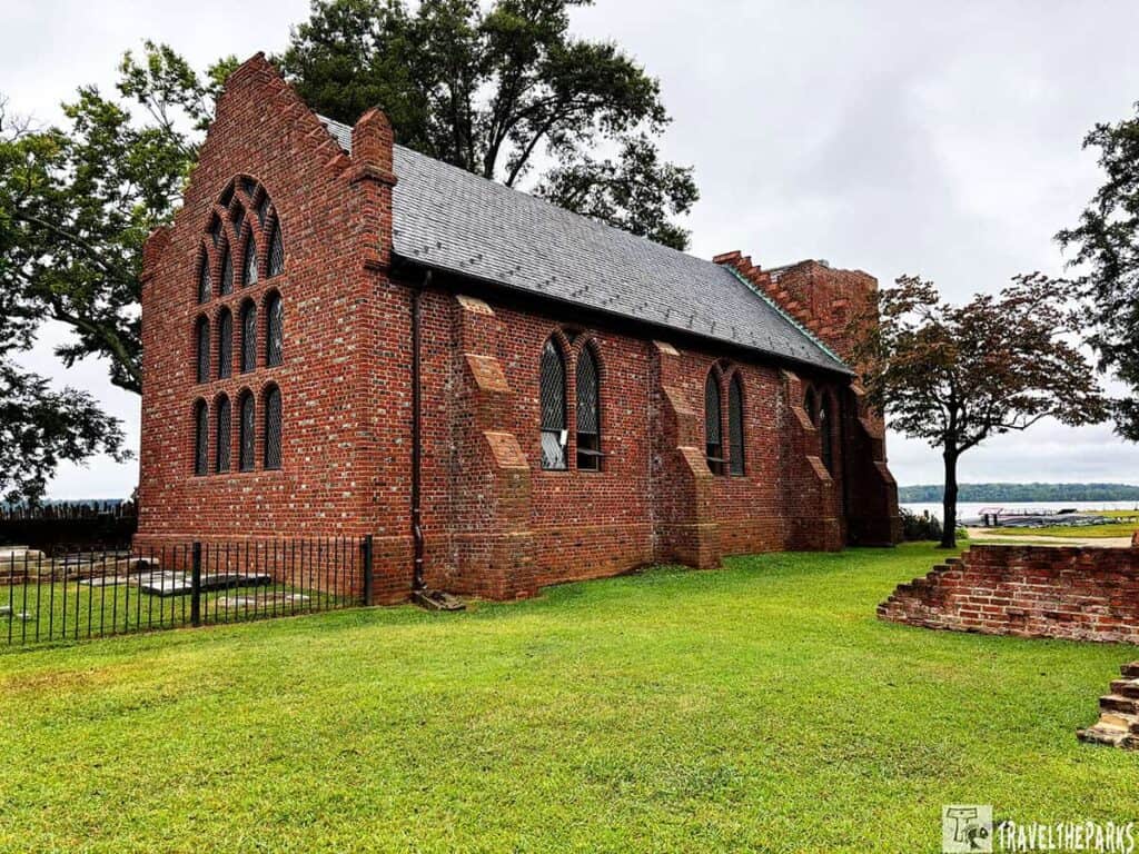 1907 Memorial Brick church with arched windows and a gabled roof in a grassy area near water.
