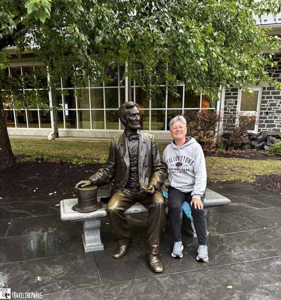 A person sitting next to a bronze statue on a stone bench in front of a building with large windows.