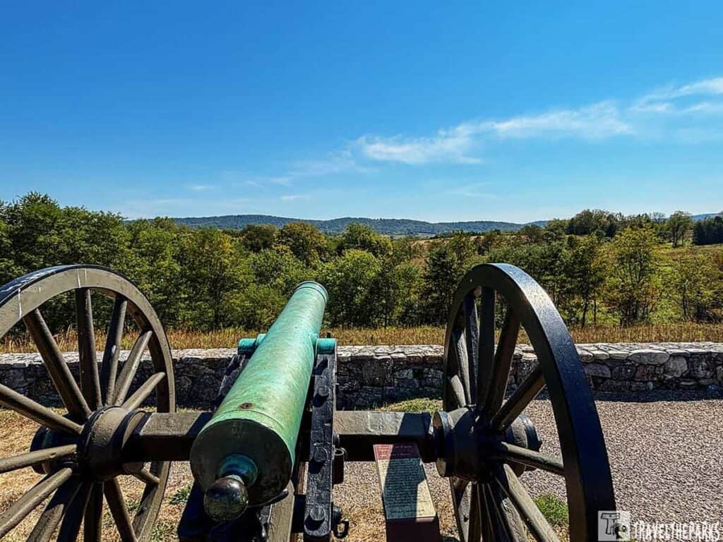 A historic cannon at Antietam National Battlefield overlooking a landscape of trees and hills under a blue sky.