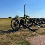 Row of historic cannons at Antietam National Battlefield with a monument and clear blue sky in the background.