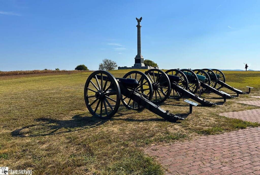 Row of historic cannons at Antietam National Battlefield with a monument and clear blue sky in the background.