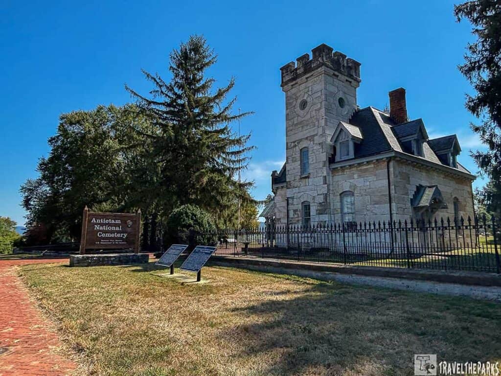Historic stone building at Antietam National Cemetery with a tower, surrounded by a black iron fence and trees.