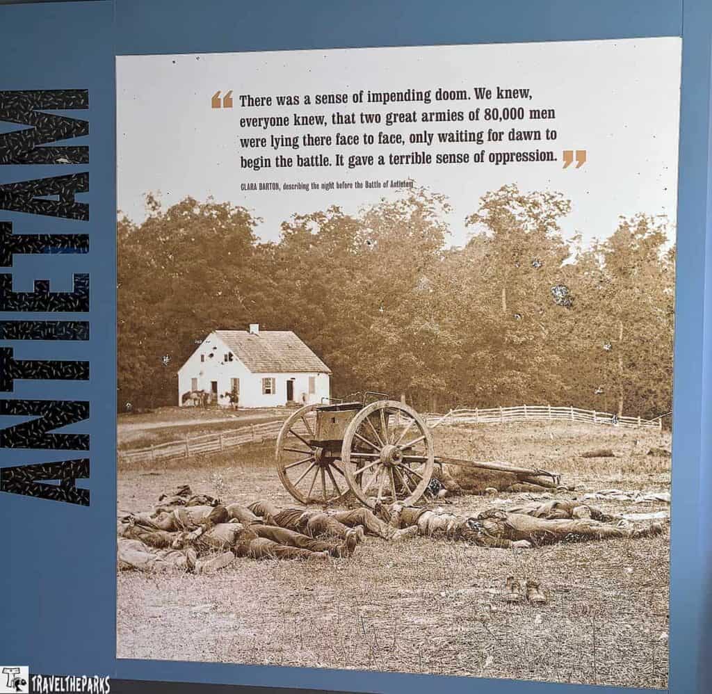 Sepia-toned image of fallen soldiers near a cannon wheel at Antietam, with a white house and trees in the background.

