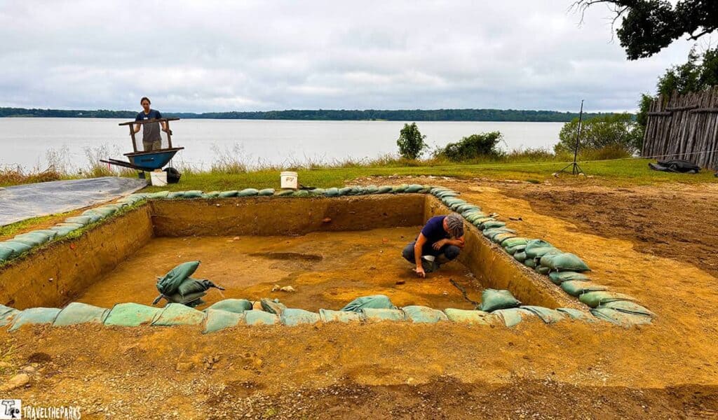 Archaeological dig site at Historic Jamestowne by a waterfront, featuring an excavation pit and two people working.