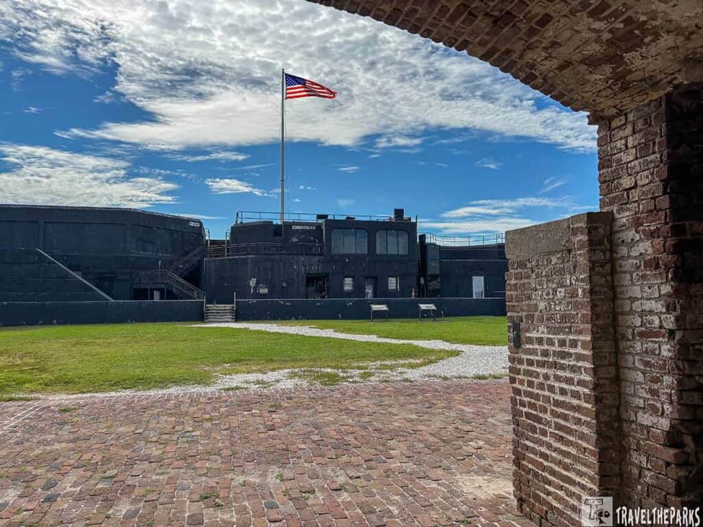 Brick archway view of Battery Isaac Huger at Fort Sumter, featuring an American flag, grass, and a blue sky.
