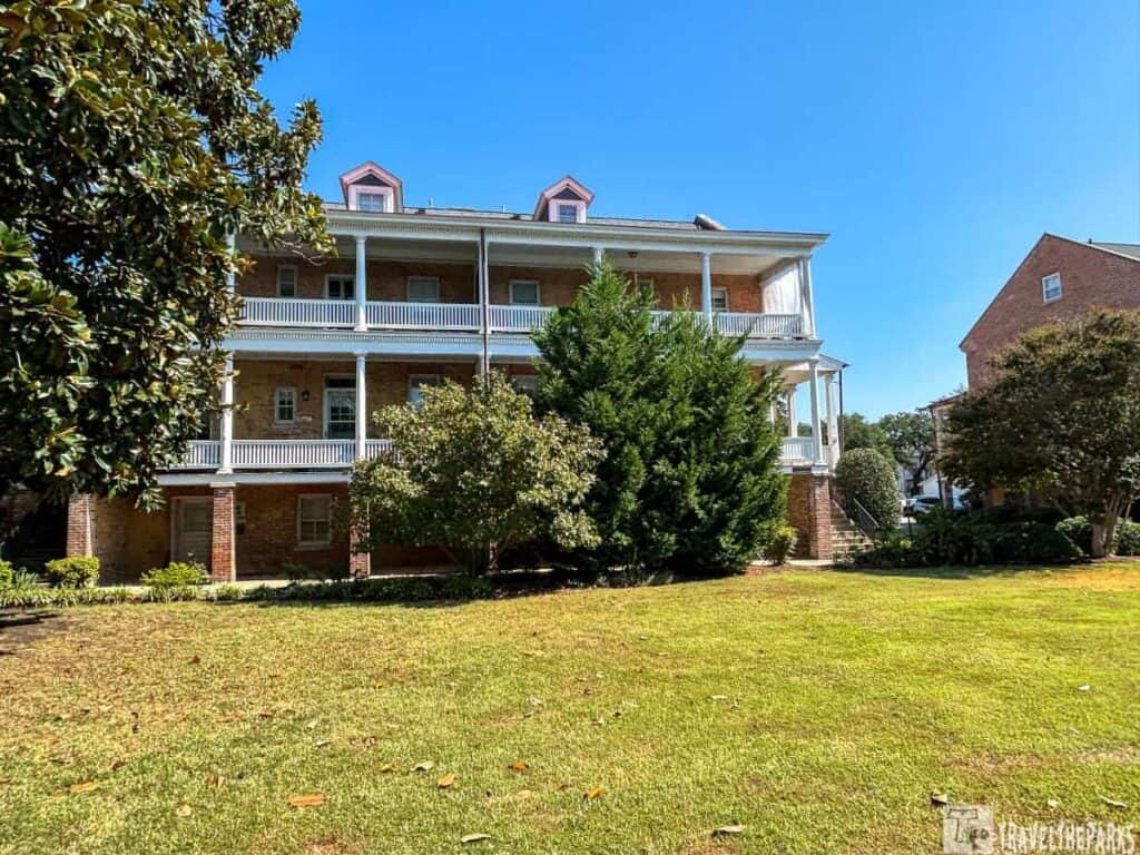 A three-story brick building with white-columned porches and a manicured lawn, under a clear blue sky.