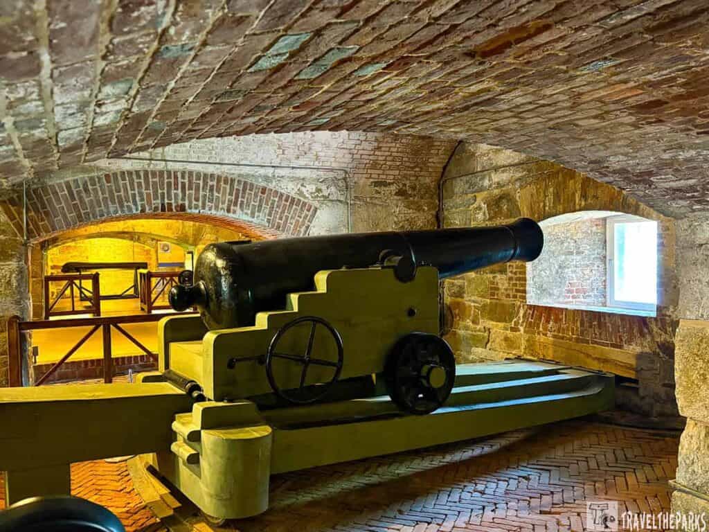 A historic black cannon on a wooden carriage inside Fort Monroe, with brick walls and arched ceiling.