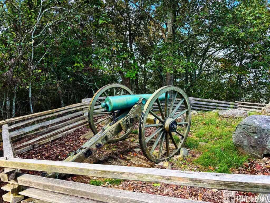 A historic cannon with a blue-green barrel and wooden carriage, surrounded by a split-rail fence at Kennesaw Mountain National Battlefield Park.
