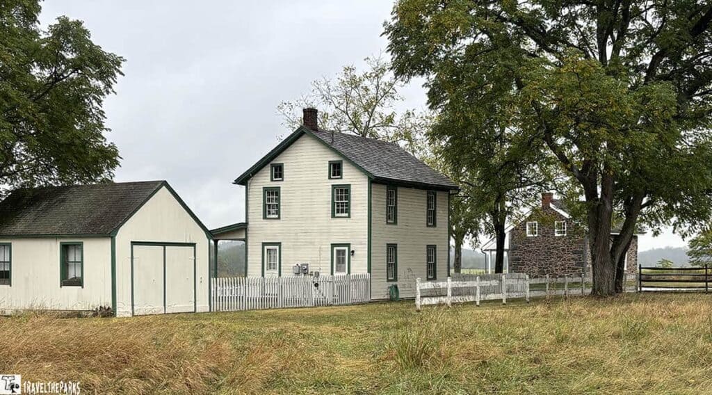 Historic farmhouse and stone building with surrounding trees and a grassy field.