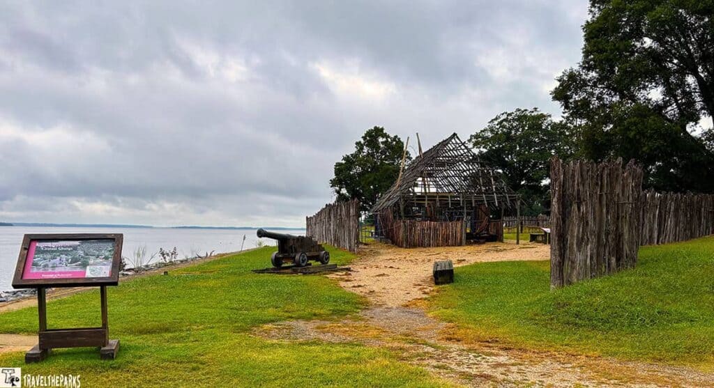 Historic Jamestowne fort with a cannon, wooden structure, and informational sign under an overcast sky.