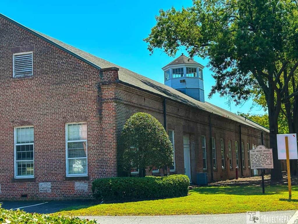 A brick building with tall windows and a rooftop structure; a bush and tree add greenery.