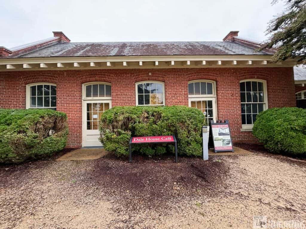 Front view of the Dale House Café, a red brick building with white-trimmed windows and bushes in Historic Jamestowne.