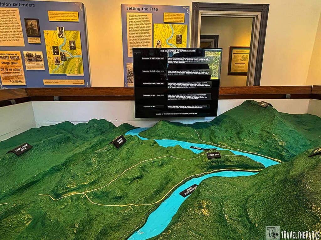 3D model of Harpers Ferry with labeled topographic features and informational panels in the background.