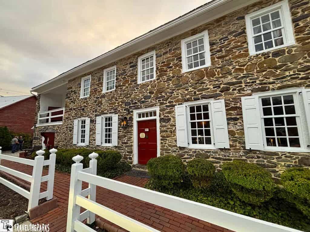 Historic stone Dobbins House building with white shutters and red door, surrounded by a white picket fence and brick pathway.