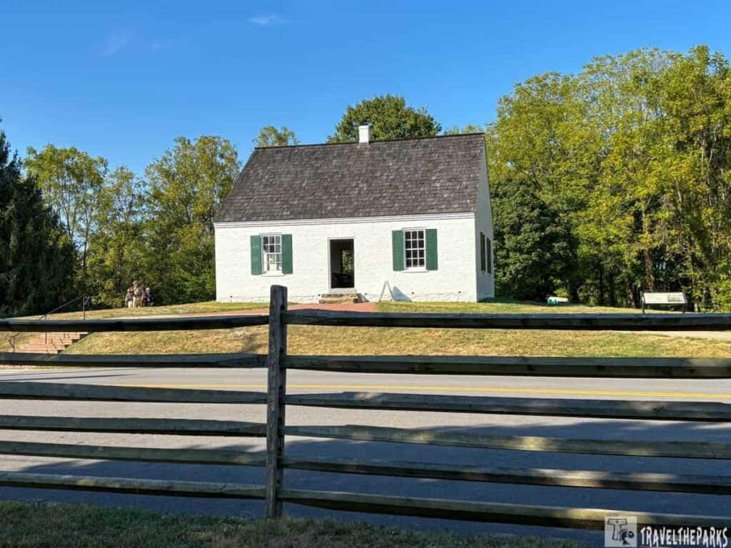 Dunker Church with a white facade and green shutters, surrounded by trees and a wooden fence in the foreground.