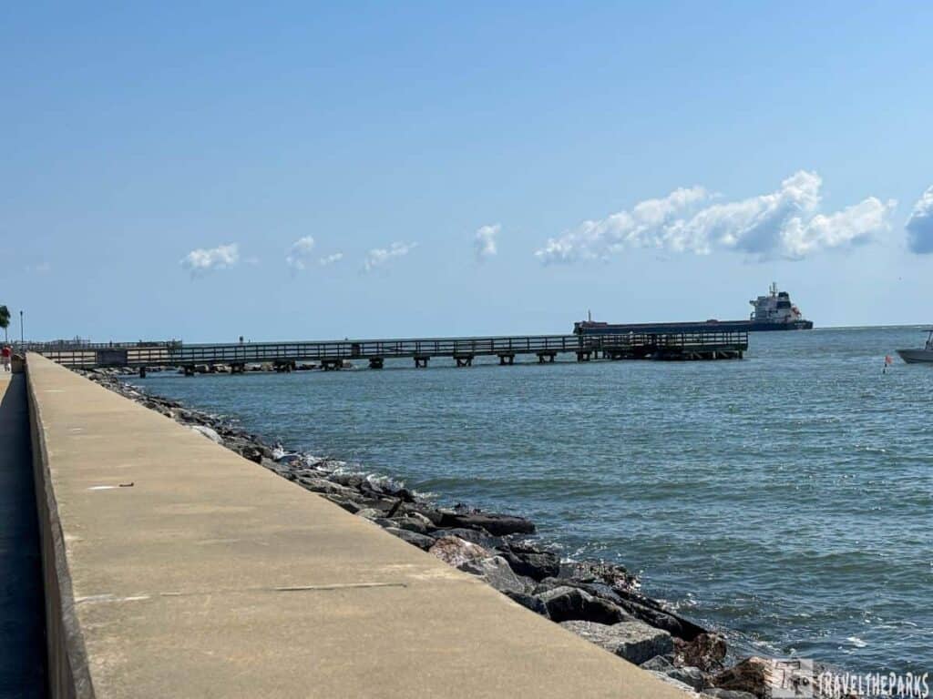 Coastal scene at Engineers Wharf-Fort Monroe with a seawall, pier, and a ship on the horizon.